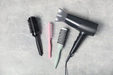 Photo of Stylish round brushes and hairdryer on light grey table, flat lay