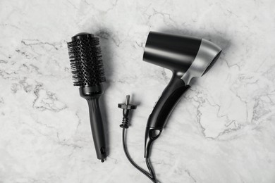 Photo of Stylish round brush and hairdryer on white marble table, flat lay