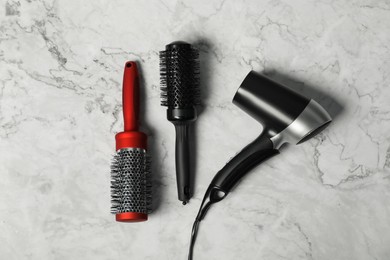 Photo of Stylish round brushes and hairdryer on white marble table, flat lay