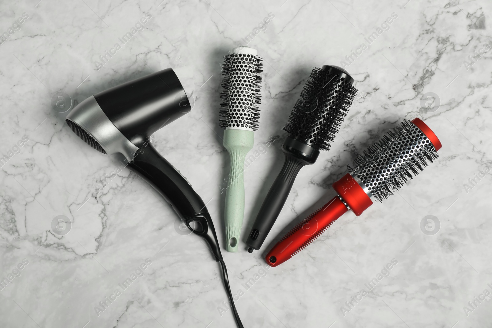 Photo of Stylish round brushes and hairdryer on white marble table, flat lay