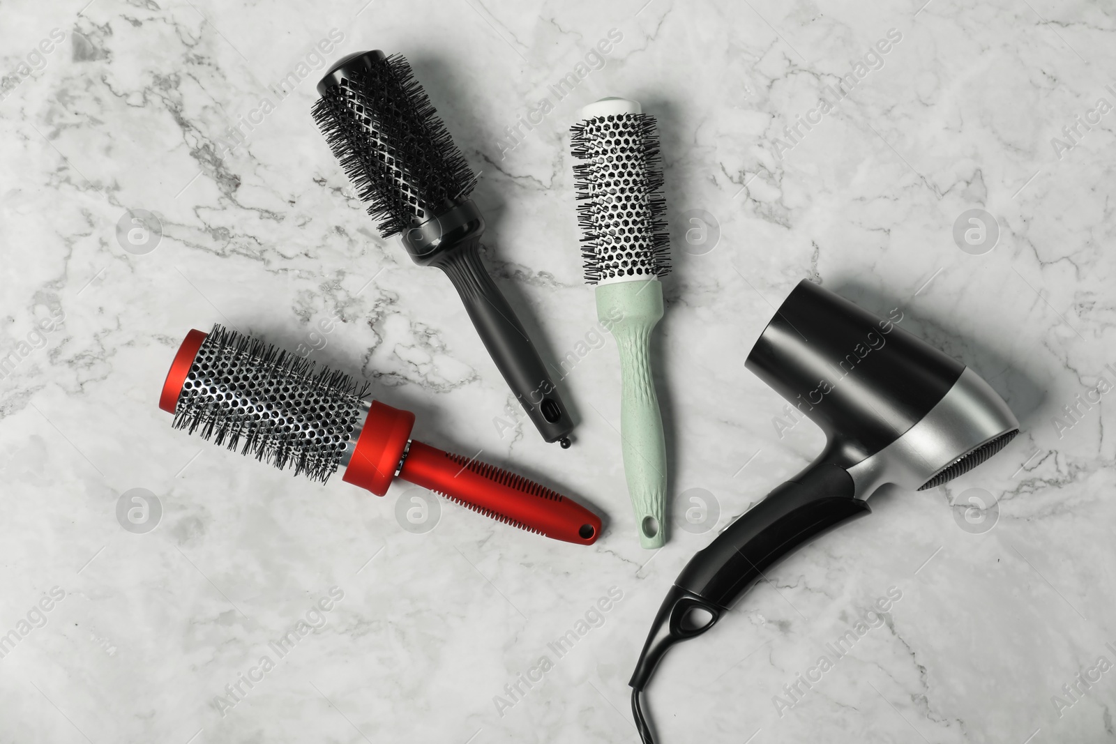 Photo of Stylish round brushes and hairdryer on white marble table, flat lay