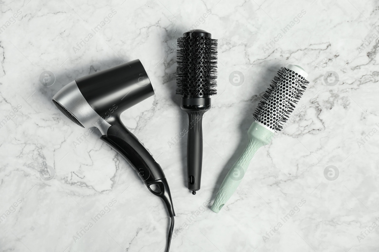 Photo of Stylish round brushes and hairdryer on white marble table, flat lay