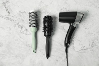 Photo of Stylish round brushes and hairdryer on white marble table, flat lay