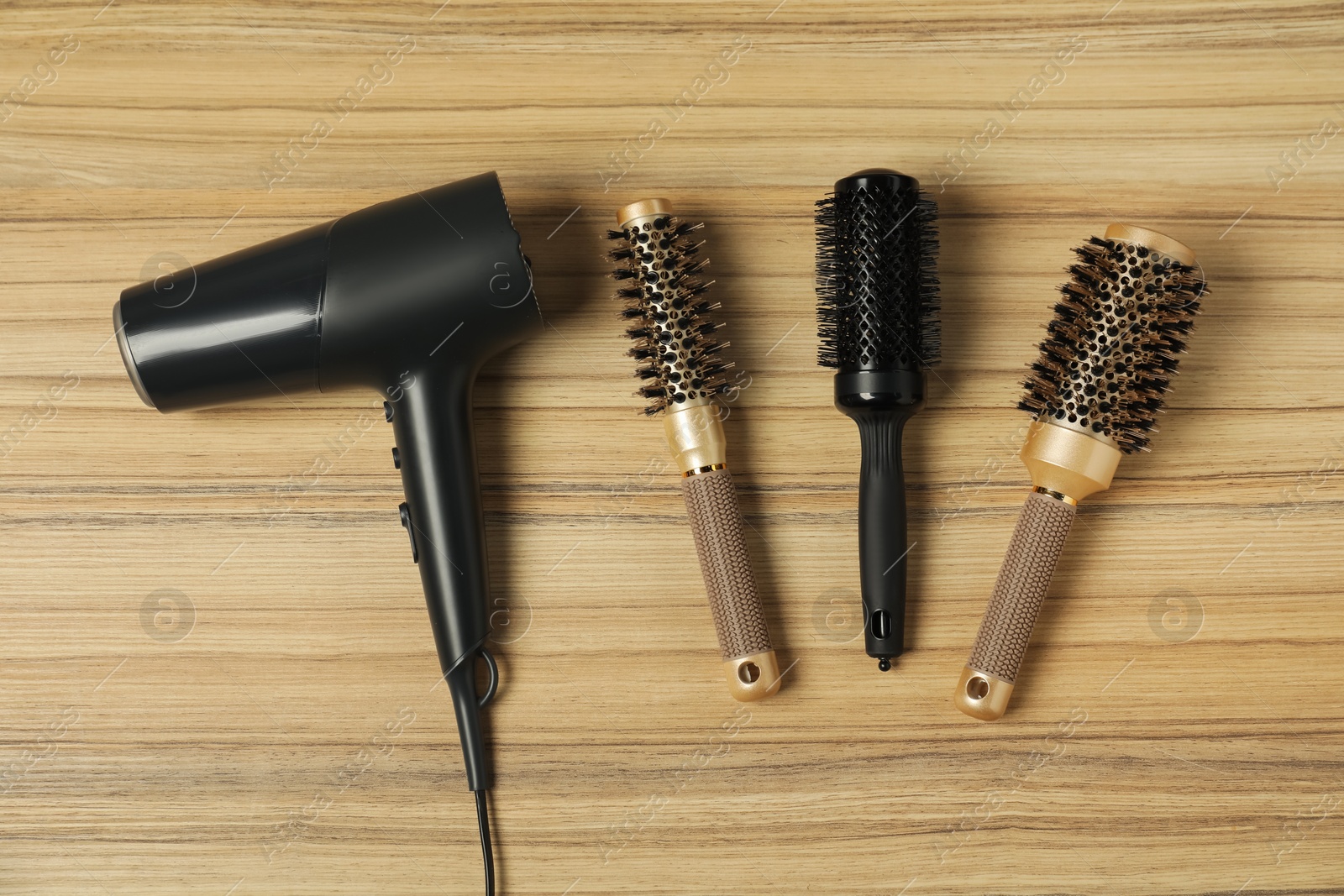 Photo of Stylish round brushes and hairdryer on wooden table, flat lay