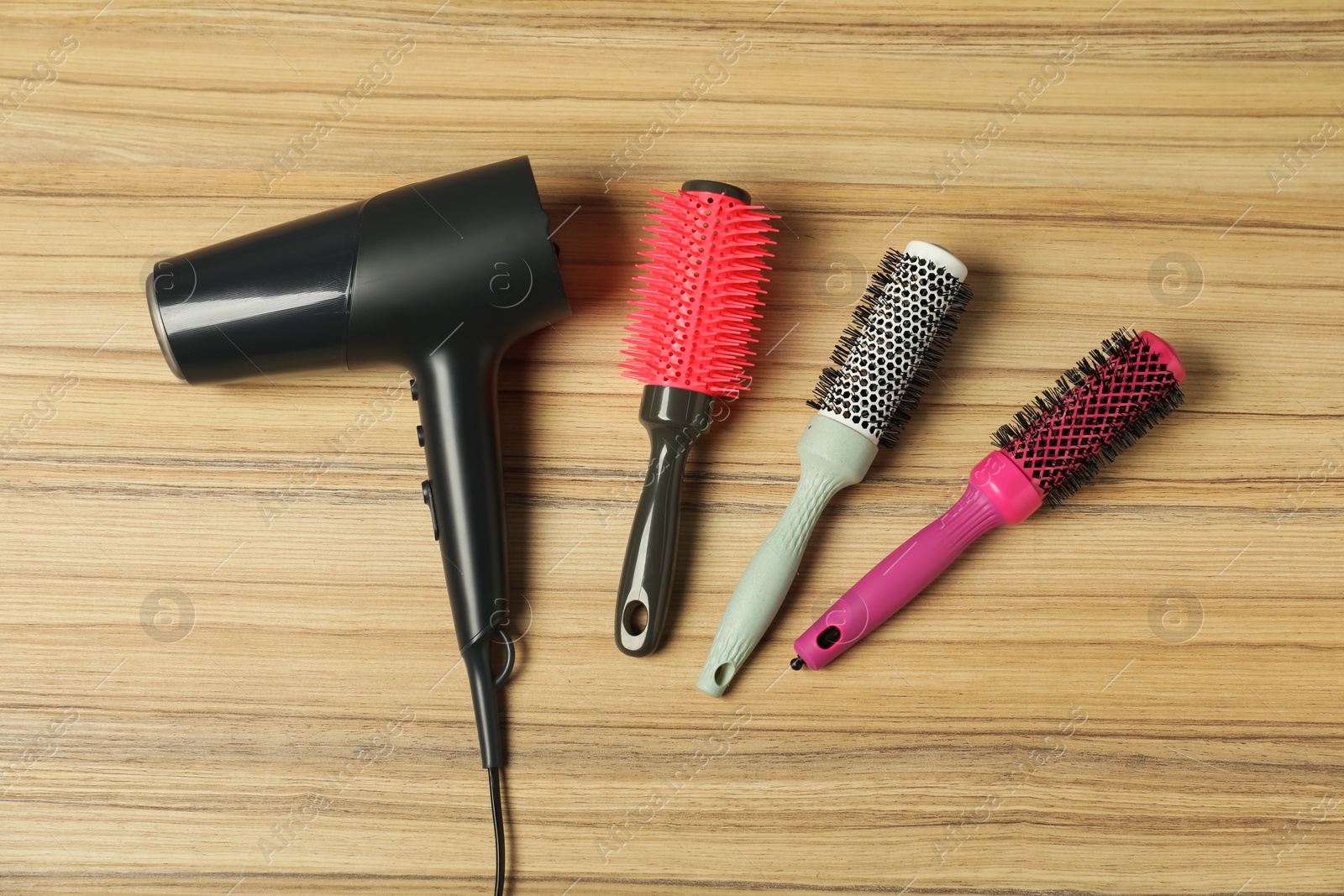 Photo of Stylish round brushes and hairdryer on wooden table, flat lay