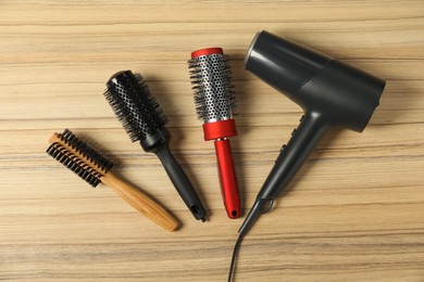 Photo of Stylish round brushes and hairdryer on wooden table, flat lay