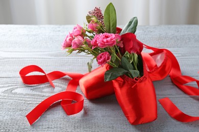 Photo of Pair of red pointe shoes and flowers on grey wooden table