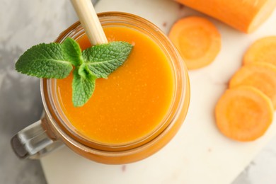 Photo of Fresh carrot juice with mint in mason jar and vegetable on gray table, top view