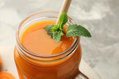 Photo of Fresh carrot juice and mint in mason jar on gray table, closeup