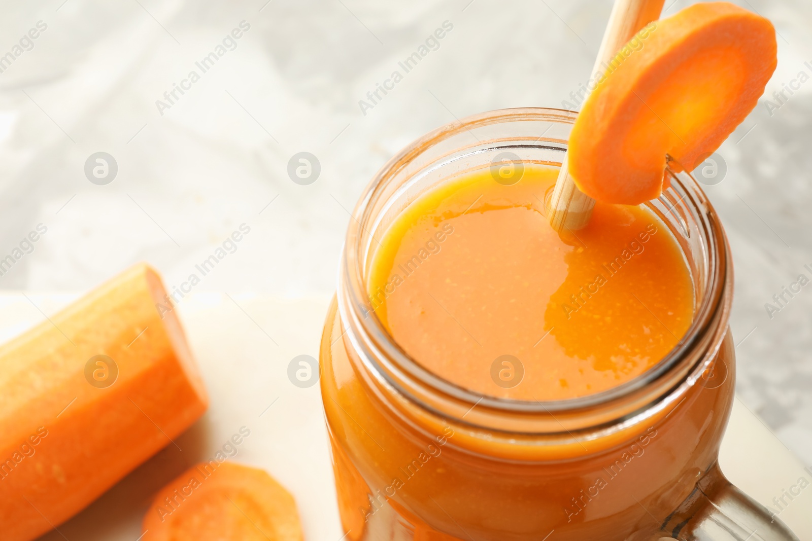 Photo of Fresh carrot juice in mason jar on gray table, closeup