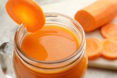 Photo of Fresh carrot juice in mason jar on gray table, closeup