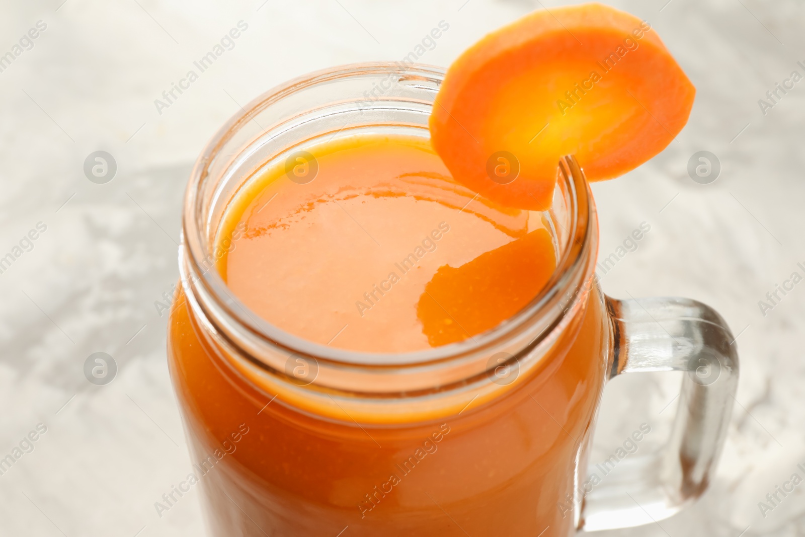 Photo of Fresh carrot juice in mason jar on gray table, closeup