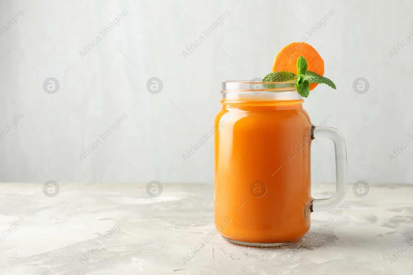 Photo of Fresh carrot juice and mint in mason jar on gray textured table, space for text