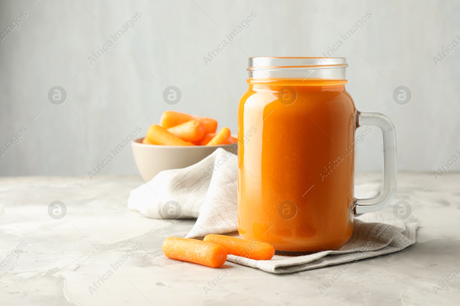 Photo of Fresh carrot juice in mason jar and vegetables on gray textured table