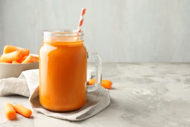 Photo of Fresh carrot juice in mason jar and vegetables on gray textured table, space for text