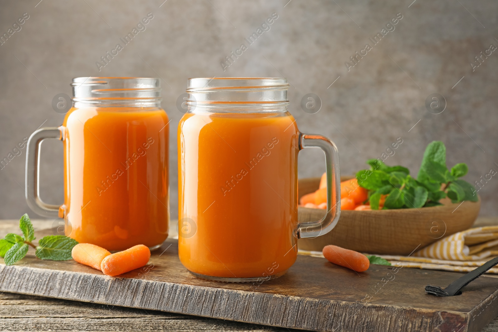 Photo of Fresh carrot juice in mason jars, vegetables and mint on wooden table against gray background