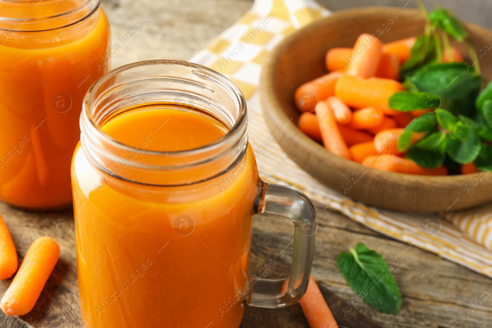 Photo of Fresh carrot juice in mason jars, vegetables and mint on wooden table, closeup