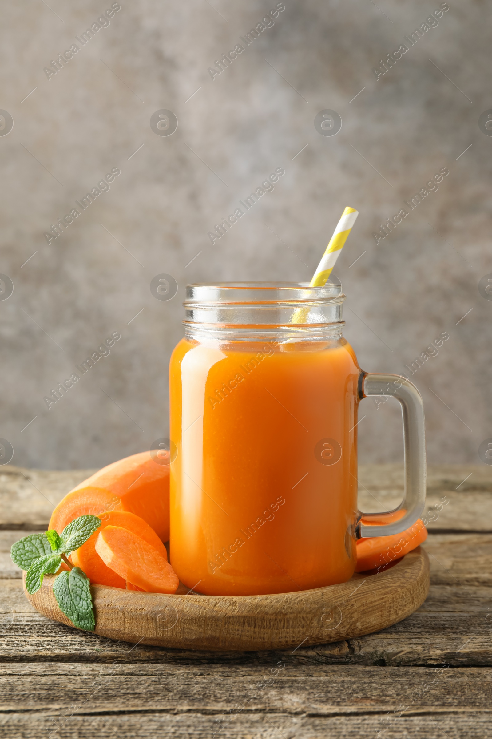 Photo of Fresh carrot juice in mason jar, vegetable and mint on wooden table against gray background