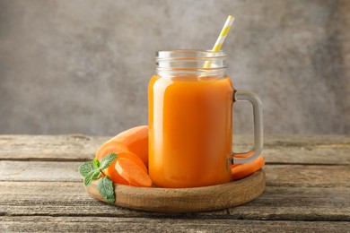 Photo of Fresh carrot juice in mason jar, vegetable and mint on wooden table against gray background