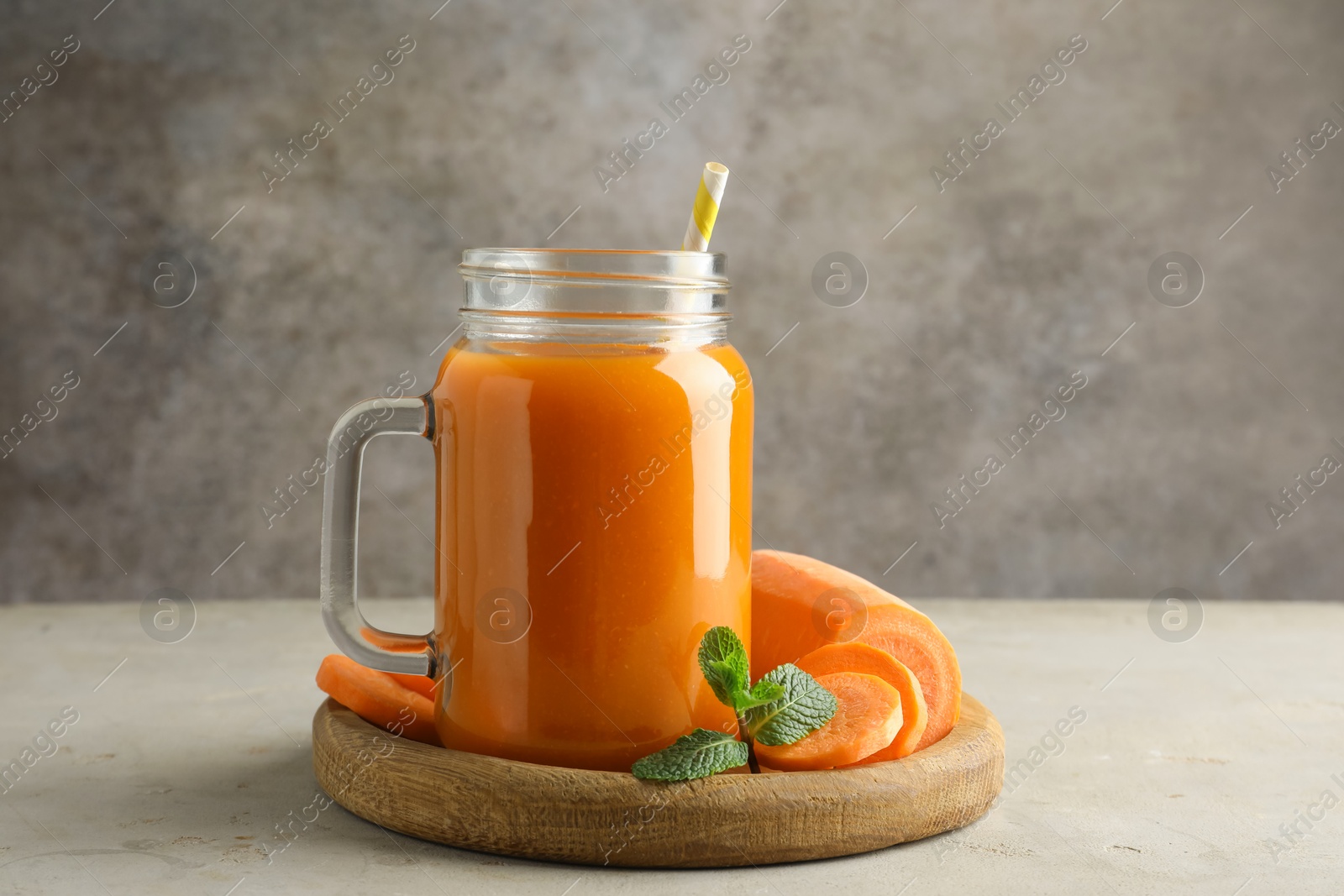 Photo of Fresh carrot juice in mason jar, vegetable and mint on gray textured table