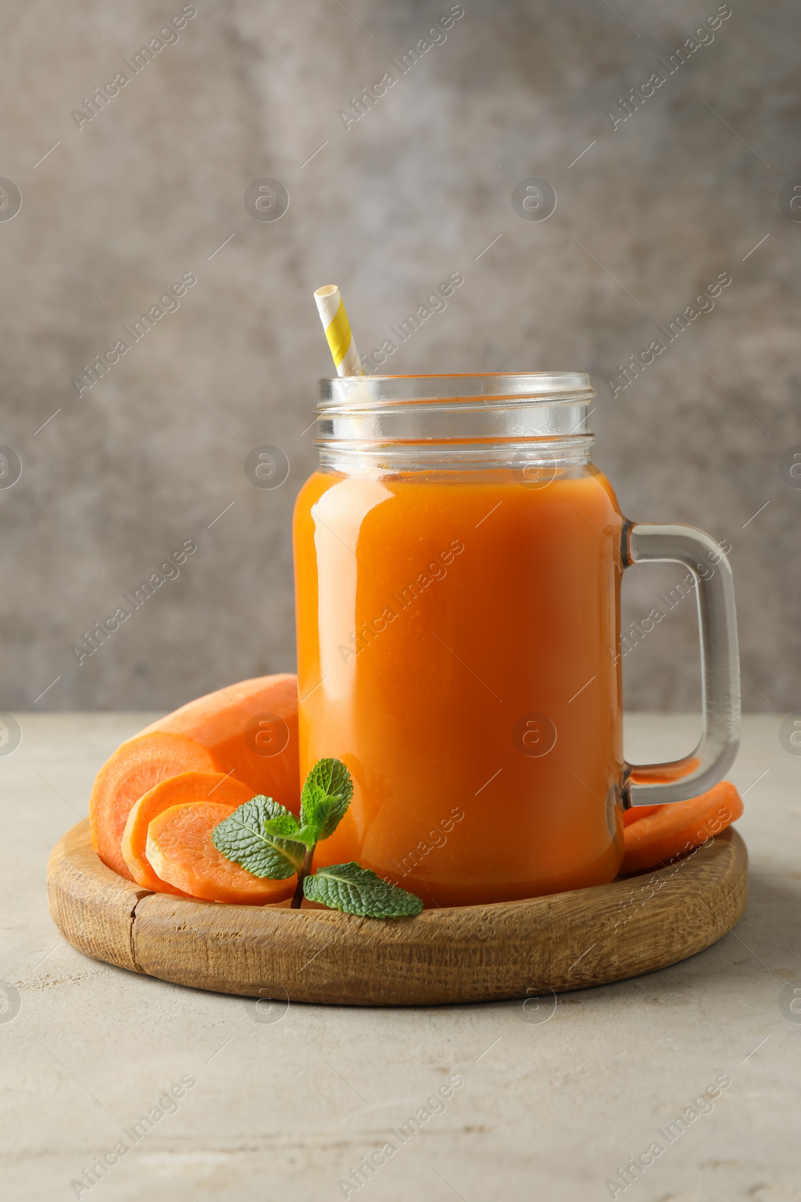 Photo of Fresh carrot juice in mason jar, vegetable and mint on gray textured table