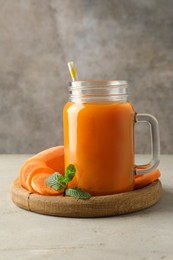 Photo of Fresh carrot juice in mason jar, vegetable and mint on gray textured table