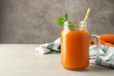 Photo of Fresh carrot juice and mint in mason jar on gray textured table, space for text