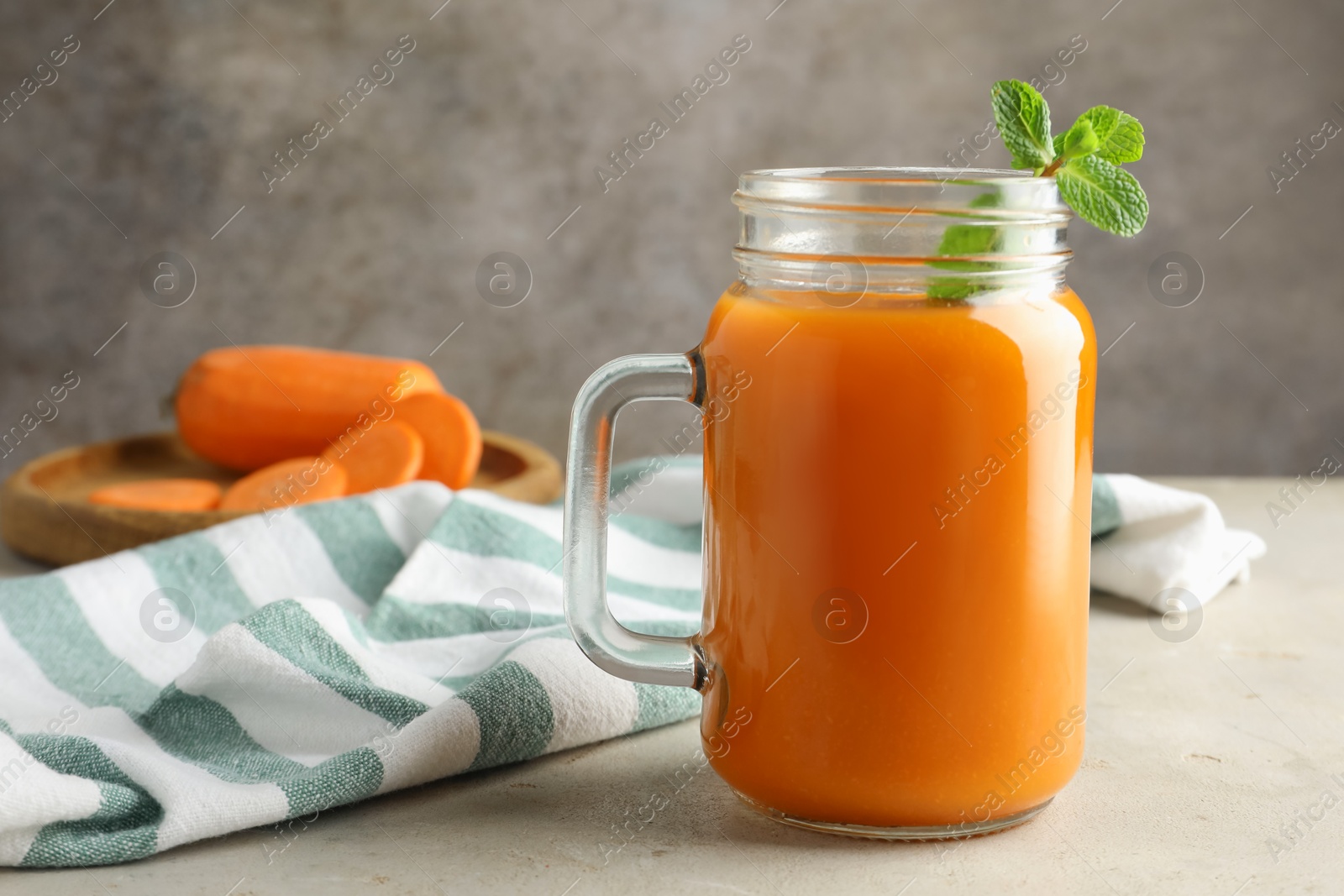 Photo of Fresh carrot juice and mint in mason jar on gray textured table