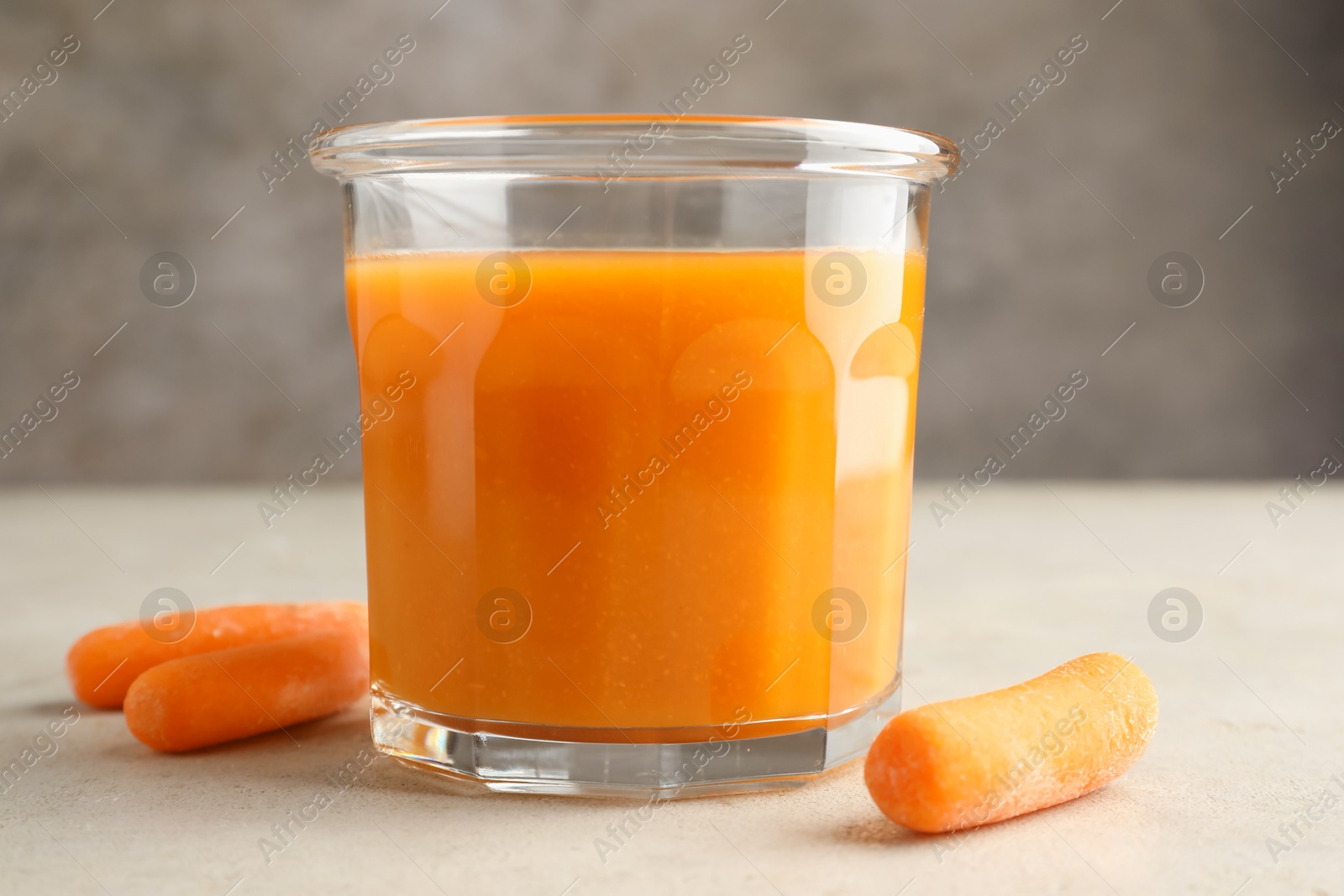 Photo of Fresh carrot juice in glass and vegetables on gray textured table, closeup