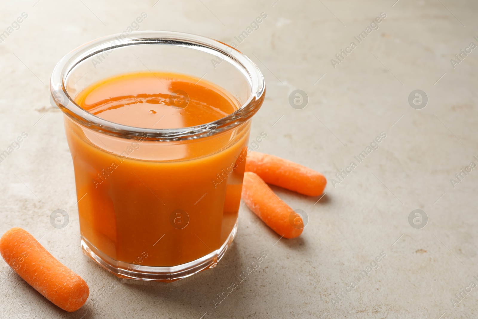 Photo of Fresh carrot juice in glass and vegetables on gray textured table, space for text