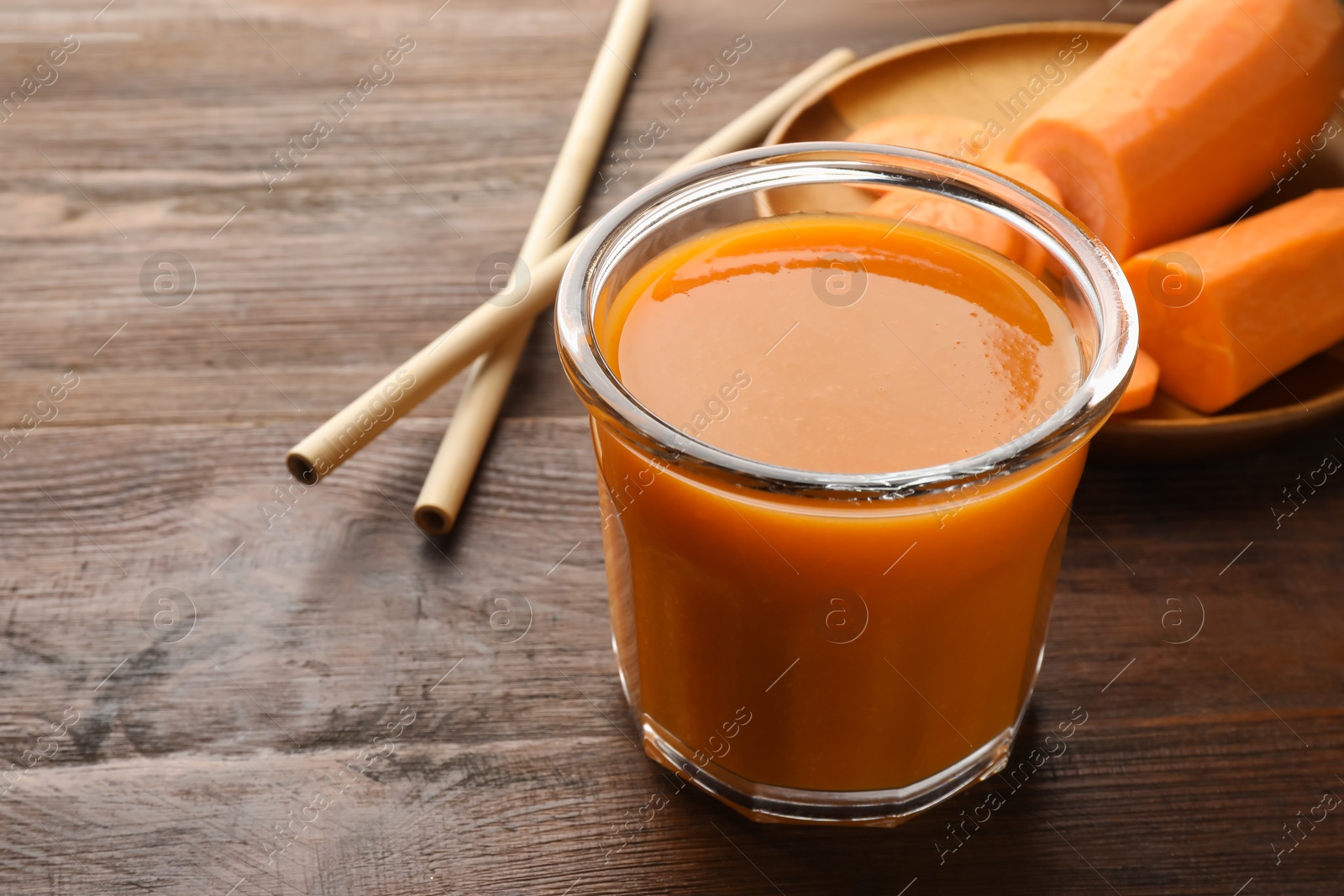 Photo of Fresh carrot juice in glass, vegetables and straws on wooden table