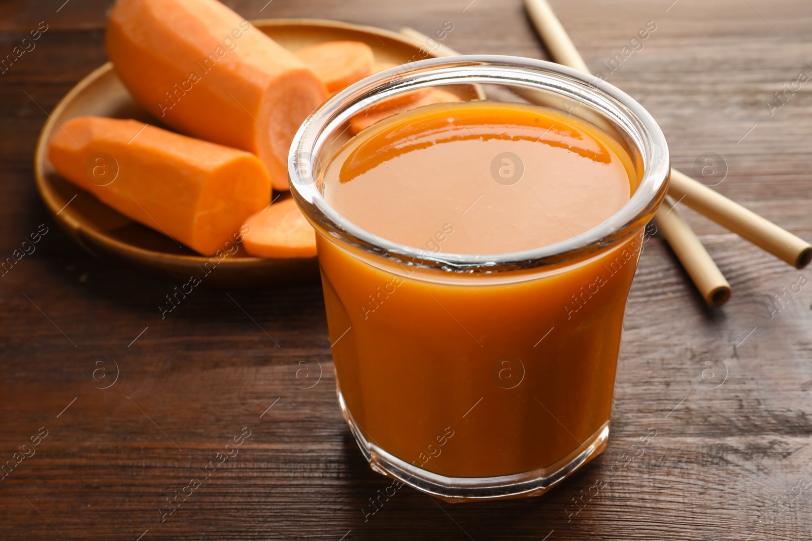 Photo of Fresh carrot juice in glass, vegetables and straws on wooden table, closeup