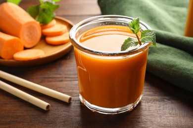 Photo of Fresh carrot juice in glass, vegetables, mint and straws on wooden table