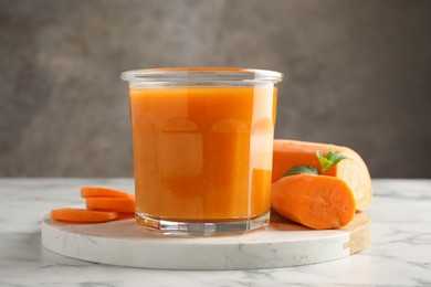 Photo of Fresh carrot juice in glass and vegetables on white marble table against gray background, closeup