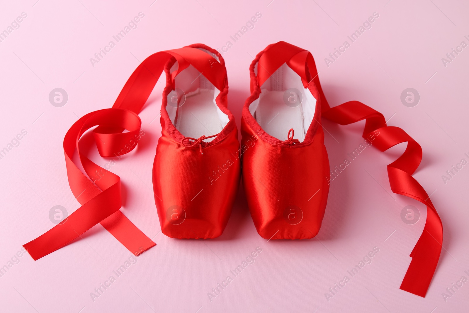 Photo of Pair of beautiful red pointe shoes on pink background