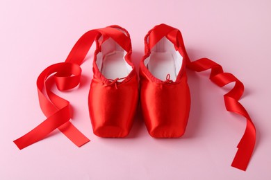 Photo of Pair of beautiful red pointe shoes on pink background