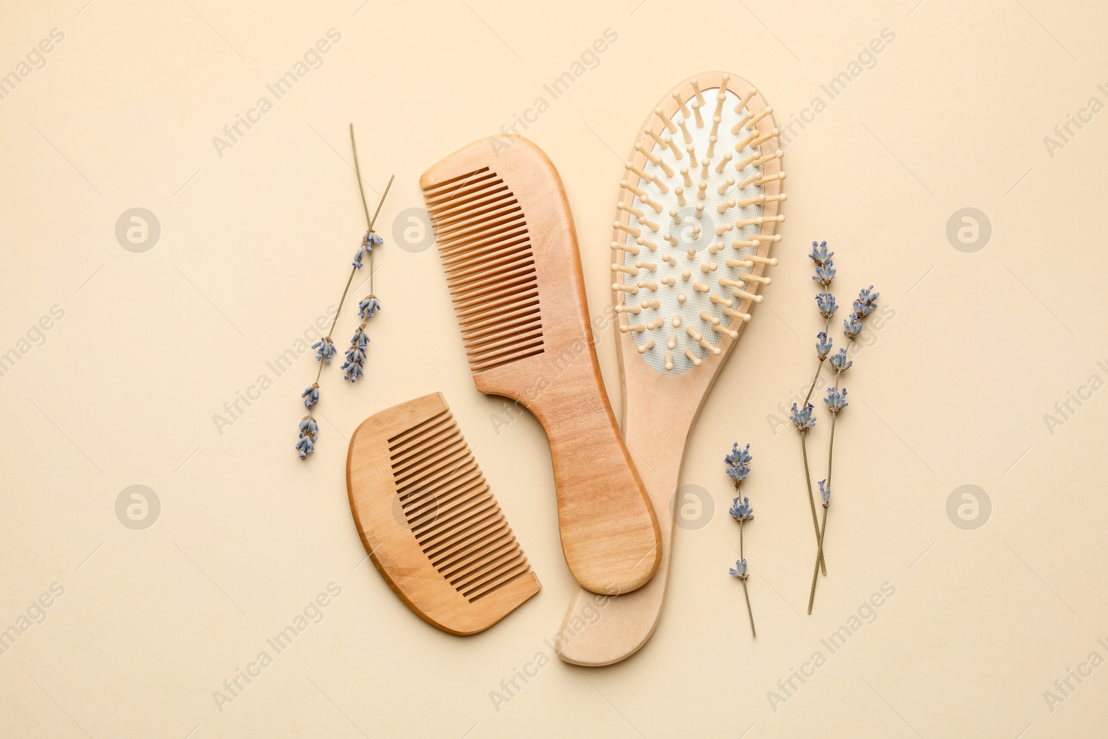 Photo of Wooden hair brush, combs and lavender flowers on beige background, flat lay