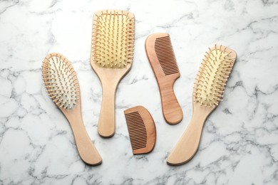 Photo of Wooden hair brushes and combs on white marble background, flat lay