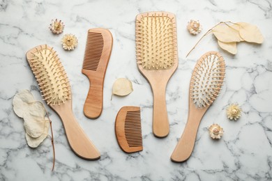 Photo of Wooden hair brushes, combs and plants on white marble background, flat lay