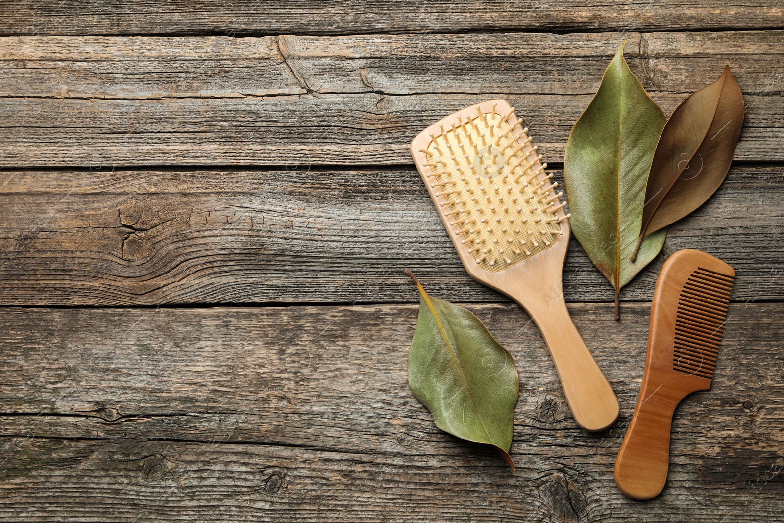 Photo of Hair brush, comb and leaves on wooden background, flat lay. Space for text