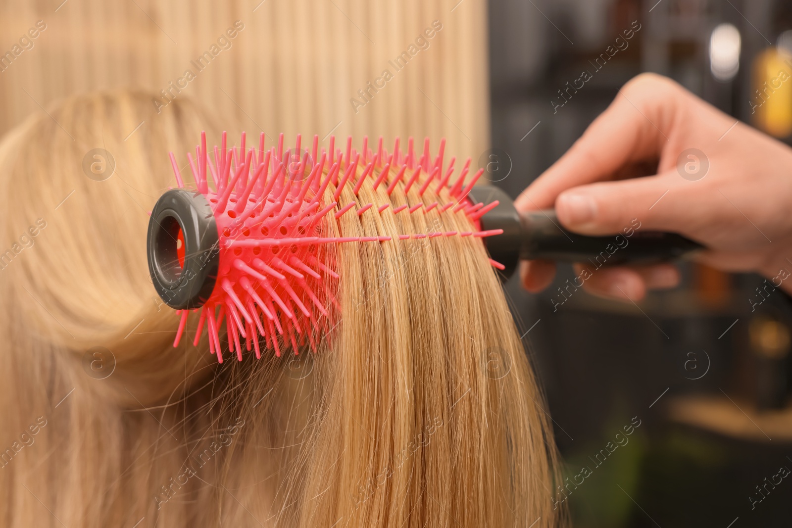 Photo of Hairdresser styling client's hair with round brush in salon, closeup