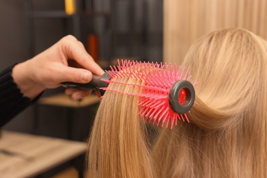 Photo of Hairdresser styling client's hair with round brush in salon, closeup