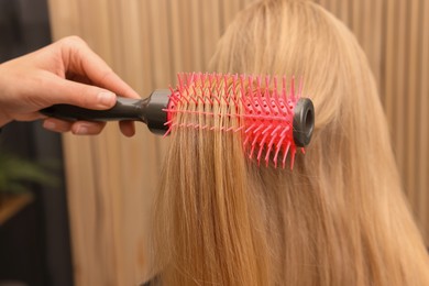 Photo of Hairdresser styling client's hair with round brush in salon, closeup