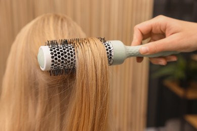 Photo of Hairdresser styling client's hair with round brush in salon, closeup