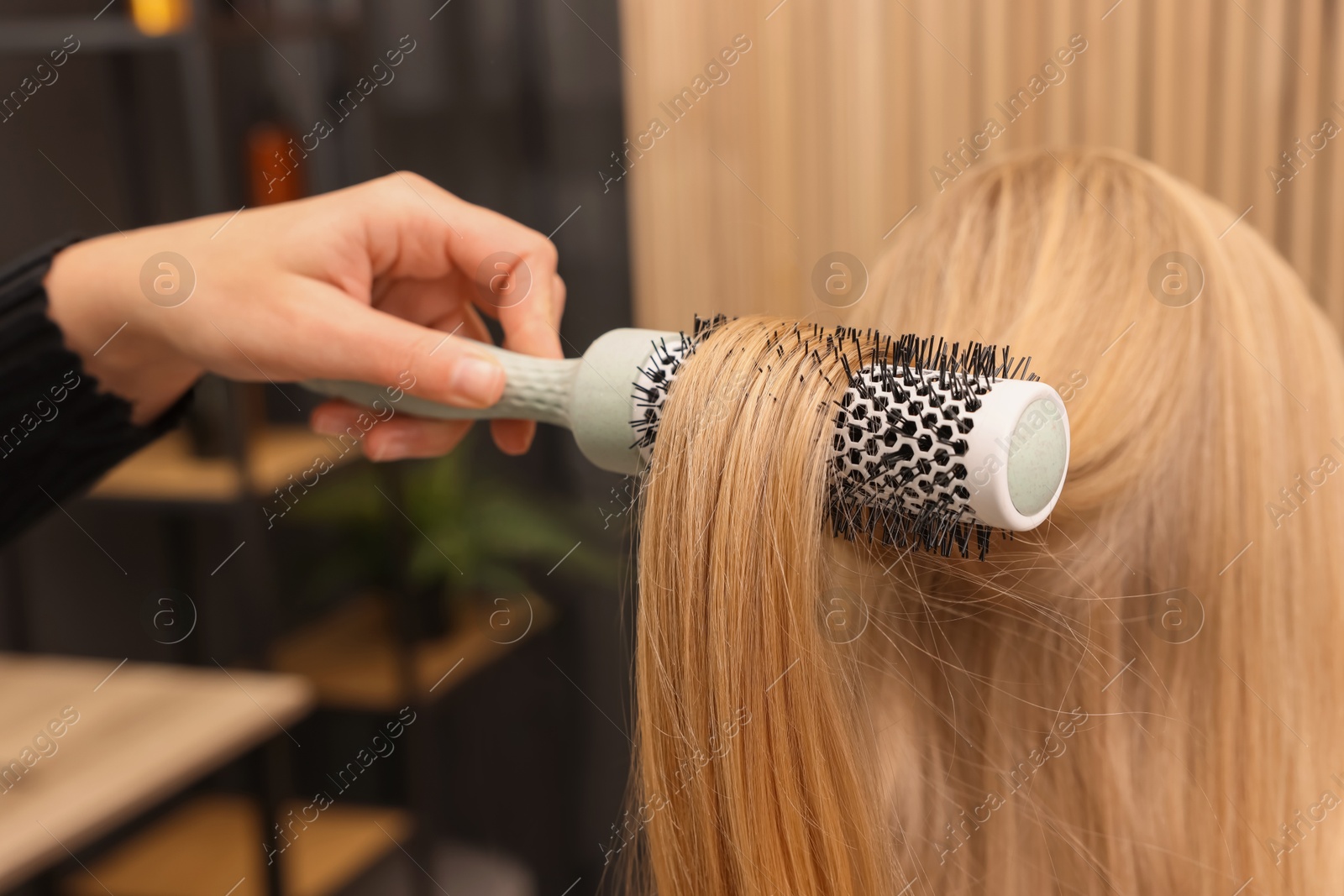 Photo of Hairdresser styling client's hair with round brush in salon, closeup