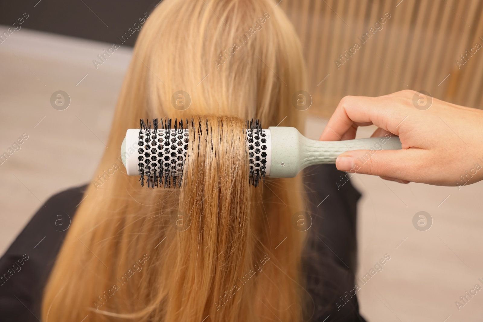 Photo of Hairdresser styling client's hair with round brush in salon, closeup