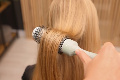 Photo of Hairdresser styling client's hair with round brush in salon, closeup