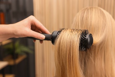 Photo of Hairdresser styling client's hair with round brush in salon, closeup