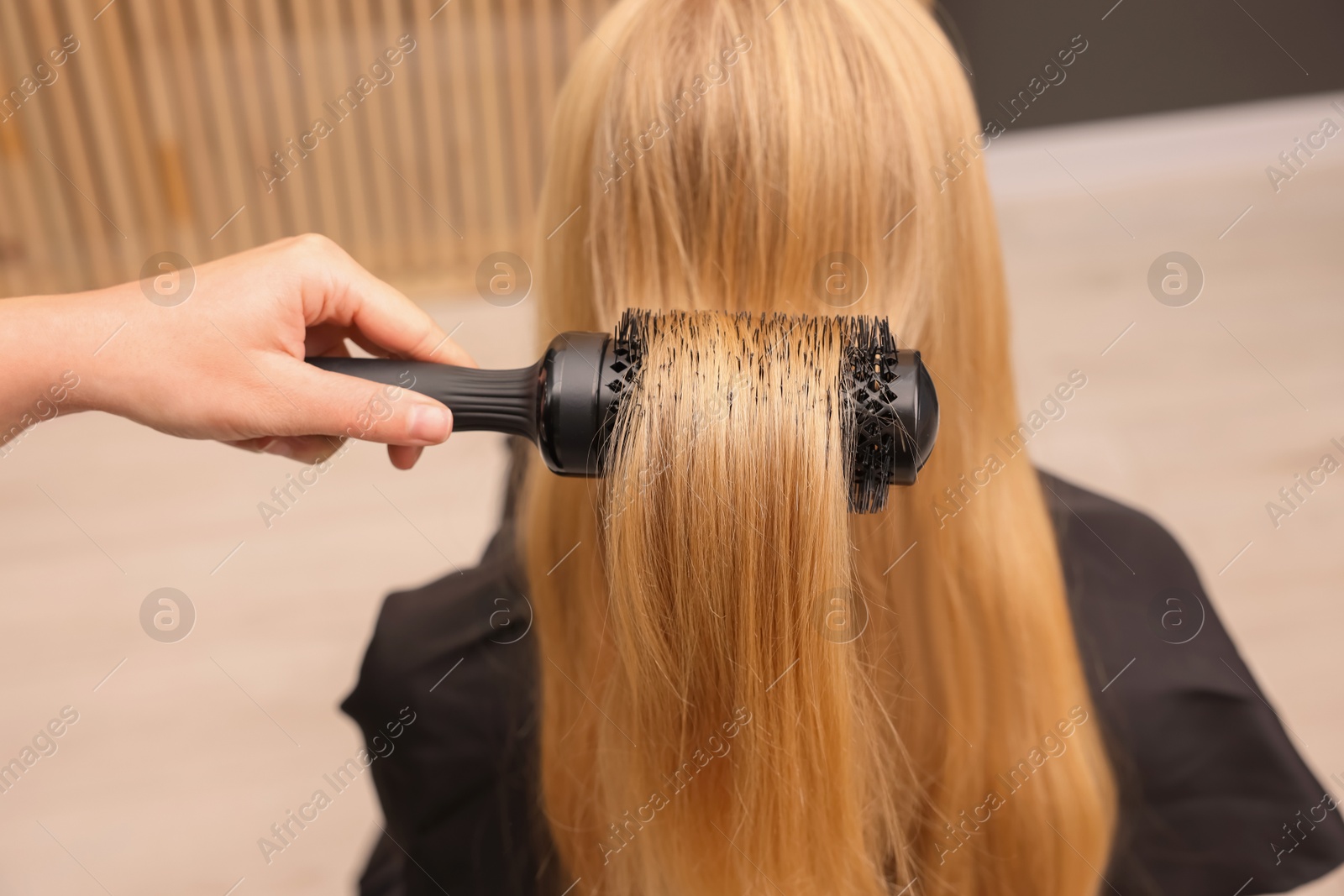 Photo of Hairdresser styling client's hair with round brush in salon, closeup