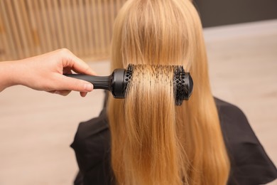 Photo of Hairdresser styling client's hair with round brush in salon, closeup